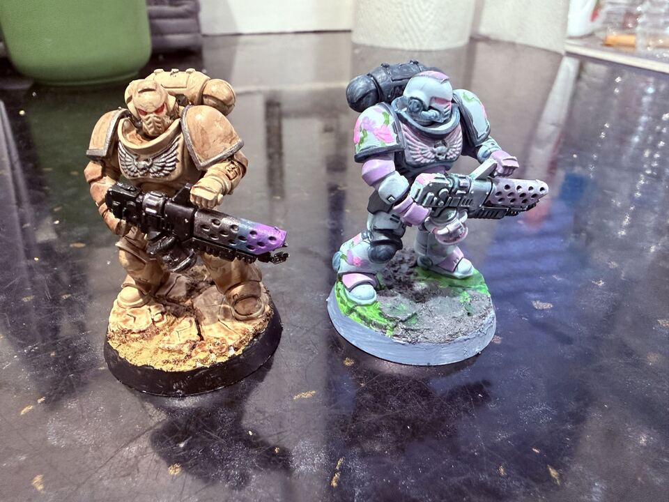 Front view of 2 painted Space Marine miniatures, one in tan and one with a flowery baby blue pattern